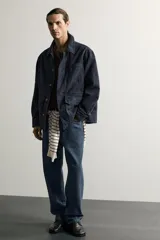 Sobrecamisa regular fit confeccionada en tejido de algodón negro con estructura canvas. Tiene cuello solapa, manga larga con puño abotonado, bolsillos de plastrón con solapa en la cadera y un bolsillo en el pecho. Cierre frontal con botones ocultos bajo solapa.