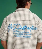 Camisa de manga corta para hombre con diseño boxy, confeccionada en tricolina de algodón con estampado de cuadros y textura sutil. Presenta cuello camisero, cierre frontal con botones y un bolsillo aplicado en el pecho.