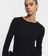 Suéter de punto color rosado, con cuello barco, mangas largas y puños con botones decorativos. El dobladillo también es acanalado.