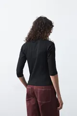 Polera de algodón color blanco, con cuello alto y mangas tres cuartos. Presenta un diseño ajustado al cuerpo con costuras decorativas en las sisas.