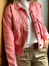 Campera rosada de gabardina con corte asimétrico, cuello clásico, cierre frontal con botones a tono, bolsillos con solapa y mangas largas.