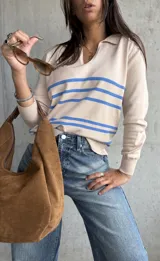 Sweater de punto fino color beige, con cuello polo y escote en V. Presenta tres rayas horizontales azules en el pecho y mangas largas con puños acanalados.