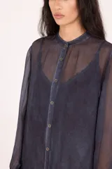 Vestido camisero largo midi de calce recto, confeccionado en tejido liviano y semitransparente, color verde oliva desgastado. Presenta cierre frontal con botones, cuello mao, mangas largas con puño y terminaciones irregulares y deshilachadas en el bajo.