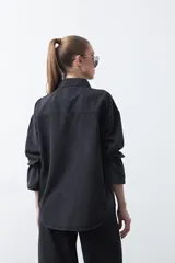 Sobrecamisa de jean negra de silueta relajada, con tachas aplicadas en líneas orgánicas que recorren la prenda. Tiene cuello camisero, cierre frontal con botones a presión y mangas largas.
