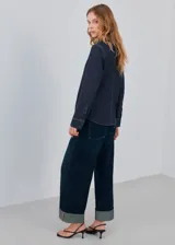 Camisa azul oscuro de denim con cuello alto y detalle de bufanda integrada en el mismo tejido.