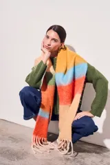 Bufanda larga tejida a rayas horizontales en tonos naranja, celeste, amarillo y beige, con flecos en los extremos.