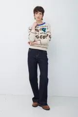 Buzo de tejido de punto en color beige con estampado de motivos florales y abstractos en tonos marrones. Presenta cuello redondo con borde en color azul vibrante, mangas largas y puños ajustados.