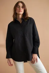 Camisa negra de corte holgado con cuello clásico, cierre frontal con botones, manga larga con puños abotonados y bolsillo de parche en el pecho.