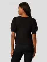 Blusa negra de corte recto con cuello redondo y mangas cortas abullonadas que presentan detalles calados con bordados en los hombros.
