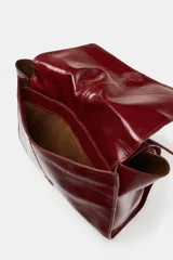 Bolso formato mini shopper de piel con acabado brillante y efecto arrugado. Cuenta con doble compartimento, cierre mediante botón imantado, bolsillo interior y asa de hombro ajustable.