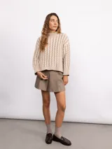 Sweater de punto con diseño de trenzas verticales, cuello alto y corte holgado. Presenta mangas largas con puños acanalados y un largo a la cadera.