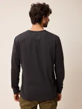 Remera de manga larga con cuello redondo y cierre frontal parcial con botones. Presenta un diseño de color sólido con un pequeño logo bordado en el pecho.