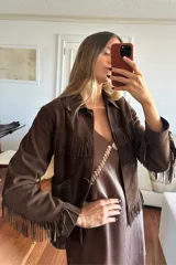 Campera de gamuza color chocolate con diseño de flecos en el pecho, espalda y mangas. Presenta cuello clásico, cierre frontal con botones y bolsillos laterales.