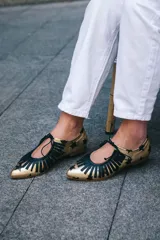 Zapatos tipo blucher artesanales de napa dorada con estampado de estrellas negras. Presentan un adorno de flecos de napa negra en el empeine, cierre con cordones y suela de cuero.