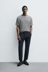 Pantalón de corte slim fit y color negro, confeccionado en tejido elástico. Cuenta con cintura elástica, trabillas, bolsillos frontales y cierre con cremallera y botón.
