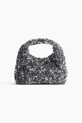 Cartera de mano con lentejuelas plateadas, asa corta y cierre magnético oculto.
