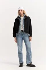 Campera de jean color negro, de calce amplio y largo a la cintura, con cuello alto y cierre frontal con broches a presión.