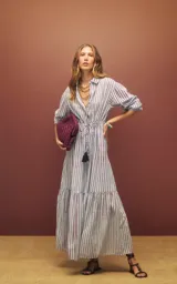 Vestido camisero largo de rayas verticales celestes y marrones, de manga larga, con cuello camisero, cierre frontal de botones y cordón ajustable con borlas en la cintura.