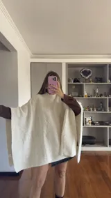 Poncho de tejido de punto en color beige, con cuello alto y diseño holgado sin mangas.