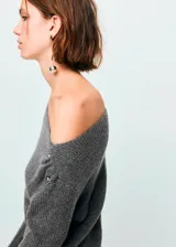 Jersey de punto medio color gris, con diseño recto, cuello barco, manga larga y bajo asimétrico. Cuenta con detalle metálico en el hombro.