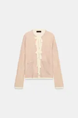 Chaqueta de punto color rosado con cuello redondo, manga larga y bolsillos delanteros. Presenta detalles de acabados con tejido combinado deshilachado en color blanco crudo y cierre frontal con lazos del mismo tono.