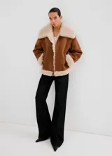 Chaqueta estilo aviador de ante sintético en color marrón con detalles de borrego sintético en el cuello, los puños, la solapa y el dobladillo inferior, con bolsillos laterales y cierre frontal con cremallera.