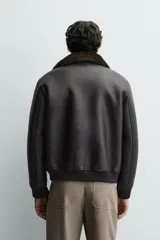 Cazadora de corte relajado confeccionada en tejido efecto piel color marrón oscuro. Presenta cuello de solapa desmontable en tejido efecto pelo, bolsillos frontales de plastrón con solapa, cierre frontal de cremallera y acabados en rib en puños y bajo.
