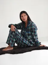 Pijama de franela a cuadros con estampado tartán, compuesto por una camisa de manga larga con solapas, bolsillo frontal y botones, y un pantalón largo de corte recto con puños y detalles en verde.