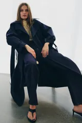 Jeans de tiro alto con corte flare y ajuste slim. Presenta trabillas en la cintura, bolsillos delanteros con detalle de botones metálicos y raya planchada a lo largo de las piernas. Cierre frontal con cremallera y botón.