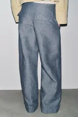 Pantalón de tiro bajo color azul con textura de lino, de pierna ancha, con bolsillos delanteros y traseros. Cierre frontal con cremallera, botón y ganchos metálicos.