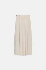 Falda larga de tiro medio, color beige claro, con caída amplia y cinturón fino negro anudado en la cintura.