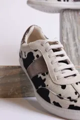 Zapatillas deportivas con estampado animal print de vaca en blanco y negro, con detalles en cuero sintético plateado en los laterales y talón.
