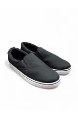 Mocasín náutico de lona color negro con bandas elásticas laterales y suela de goma blanca con línea negra.