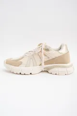 Zapatilla deportiva de diseño urbano en tonos neutros, combinando paneles de malla, gamuza y detalles metalizados en color dorado. Cuenta con suela robusta y acordonado frontal.