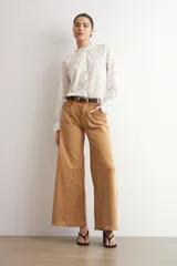 Camisa blanca de manga larga con cuello alto y volados, confeccionada en tela con bordado inglés y detalles calados verticales. Presenta puños con volados y cierre frontal con botones.
