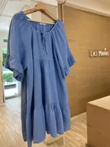 Vestido corto celeste de lino, con escote redondo con lazo, mangas cortas amplias con volados y ruedo con volados.