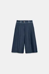 Bermuda ancha de tiro alto, confeccionada en denim color azul, con pinzas delanteras y detalles de vivos a contraste. Cuenta con cierre frontal con cremallera y botón.