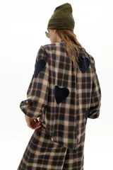 Camisa oversized de algodón con estampado de cuadros en tonos marrones y azules. Presenta cuello mao, cierre frontal con botones de nácar, mangas largas abullonadas con puños elásticos y apliques decorativos en forma de corazón de lana en el frente y las mangas.