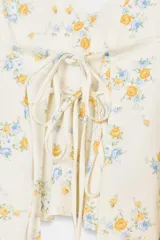 Top corto color blanco roto con estampado floral en tonos amarillo y azul. Presenta escote pico, tirantes finos ajustables y detalle de lazos en el delantero. El bajo tiene un volante.