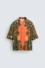 Camisa de corte relajado confeccionada en tejido fluido con mezcla de viscosa y lino. Presenta cuello bowling, manga corta y cierre frontal con botones. Diseño con estampado floral en tonos verdes y naranjas.