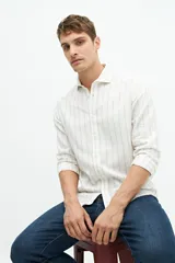 Camisa de manga larga color blanco hueso con finas rayas verticales en tono beige. Presenta cuello camisero y un pequeño logo bordado en el pecho.