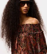 Blusa tipo bata de manga larga confeccionada en chiffon, con diseño de escote hombro a hombro con elástico y puños ajustados con detalle de frufru. Presenta un estampado paisley en tonos oscuros y rojizos.