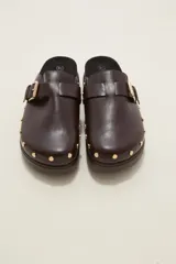 Suecos negros de estilo casual con acabado en eco cuero, detalle de hebilla metálica ajustable en el empeine y tachas decorativas en el contorno de la suela. Presentan una base de corcho y suela de goma dentada.