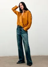 Camisa de tejido satinado en color mostaza, con diseño cruzado, cuello camisero, manga larga con puños abotonados y cierre delantero de botones ocultos.