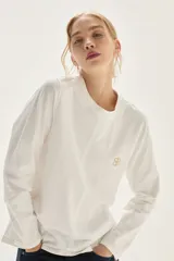 Remera de algodón de manga larga con cuello redondo, corte recto y bordado pequeño en el pecho. Presenta costuras con pespuntes a contratono en los puños y el ruedo.