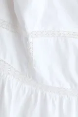 Vestido midi de algodón color blanco, con escote halter y breteles para atar en la nuca. Presenta detalles de encaje en el escote y la cintura, y falda fruncida con leve vuelo.