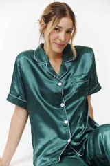 Conjunto de pijama verde esmeralda de satén con ribetes blancos, compuesto por camisa de manga corta con botones y pantalón capri.