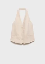 Chaleco sastrero de lino color beige, con cuello halter pronunciado y cierre frontal de cuatro botones. Presenta bolsillos ribeteados simulados en el frente y dobladillo en punta.