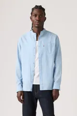 Camisa celeste de manga larga con cuello mao y cierre frontal de botones. Cuenta con un bolsillo aplicado en el pecho adornado con una pequeña etiqueta roja.