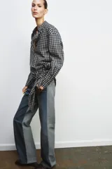 Jeans de tiro alto con diseño de paneles en contraste, combinando denim negro y gris. Presenta cinco bolsillos, cierre frontal con cremallera y botón metálico, y costuras con efecto deshilachado en la unión de los paneles.